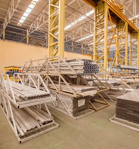 Ferme metalice și panouri stivuite într-o hală de producție, pregătite pentru montaj