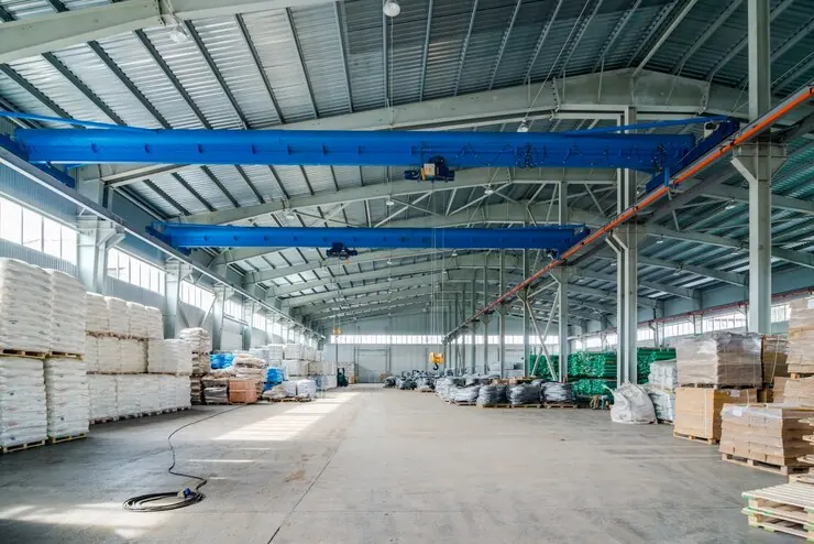 Interior de hală de producție cu pod rulant albastru și paleți cu materiale