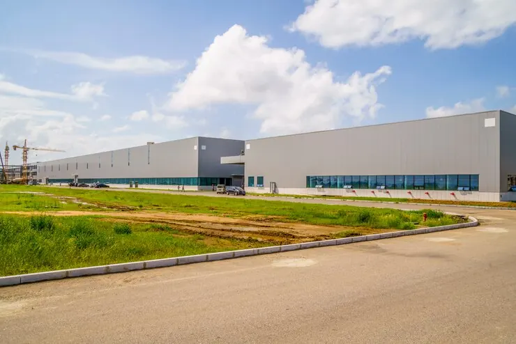 Hale industriale noi într-o zonă industrială, cu teren verde și drum de acces în față